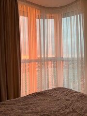 Warm sunset light filtering through sheer curtains in a cozy bedroom corner with city view