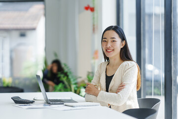 Portrait of smiling asian businesswoman sitting at desk with laptop and documents in modern office