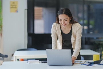 Young happy manager working on a laptop in a bright, modern office, embodying the essence of...