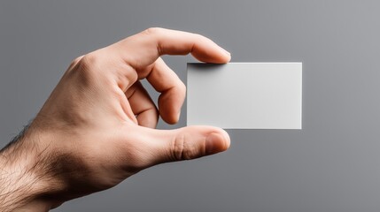 Obraz premium Hand holding blank white card in front of gray background ready for design