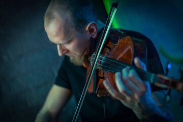 Fototapeta premium The violinist plays the violin. Brutal man with a beard playing the violin fatal simony. Close-up