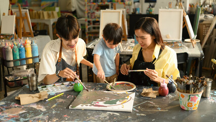 A preschool teacher assists a mother and child during an art class