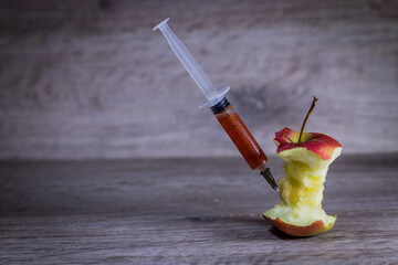 Pesticides and nitrates are injected into a bitten red apple with a syringe.