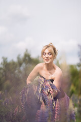 Blonde girl with a bouquet of lupines in a field walking in the summer