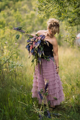 Blonde girl with a bouquet of lupines in a field walking in the summer