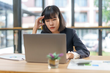 Young Asian businesswoman having headache and touching her head while working on laptop computer at...