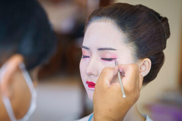 Beautiful Asian female tourist receives traditional Geisha or Maiko makeup, an ancient Japanese culture for beauty by professional make-up artist.