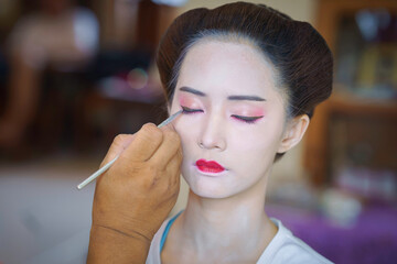 Beautiful Asian female tourist receives traditional Geisha or Maiko makeup, an ancient Japanese culture for beauty by professional make-up artist.