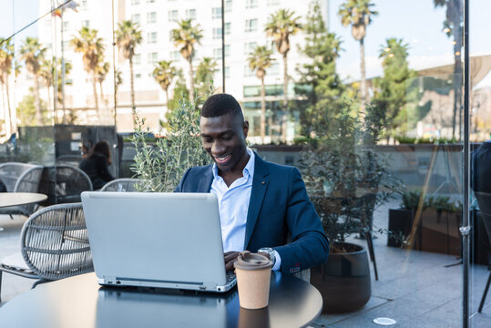Smiling African american businessman working on laptop outdoors at cafe table with coffee