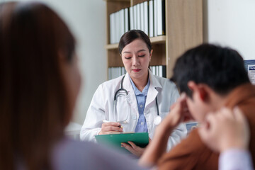 Female doctor writing on clipboard during a medical consultation with a couple in hospital office