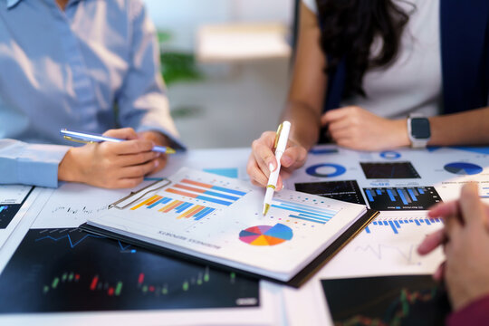 Business team engaged in analyzing marketing data and financial reports while pointing at charts and graphs with pens in a corporate office setting