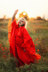 Beautiful girl in a red dress in a poppy field with a big poppy