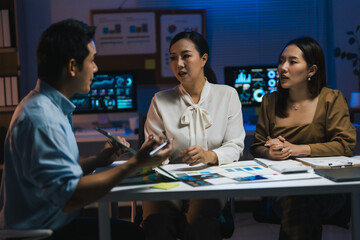 Asian businesspeople having a discussion about financial charts and graphs, working late at night in a modern office