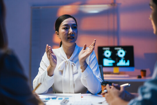 Asian businesswoman gesturing while leading a late night meeting with her colleagues in the office