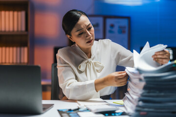 Stressed businesswoman working late into the night, surrounded by paperwork and a laptop, grappling with deadlines and mounting pressure