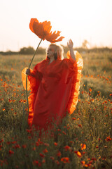 Beautiful girl in a red dress in a poppy field with a big poppy