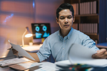 Young professional working late at night, analyzing documents and focused on a computer in a modern office environment