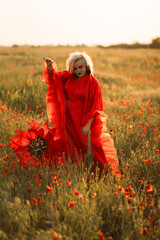 Beautiful girl in a red dress in a poppy field with a big poppy