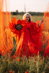 Beautiful girl in a red dress in a poppy field with a big poppy