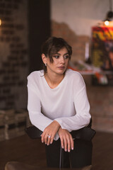 Elegant woman in white sweater leaning on chair in cozy loft interior. Soft warm lighting, thoughtful expression, stylish urban atmosphere