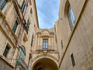 Baroque architectural detail with arched passage and balcony in historic European building under blue sky.
