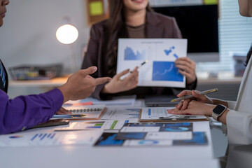 Three people are sitting at a table with papers and graphs in front of them