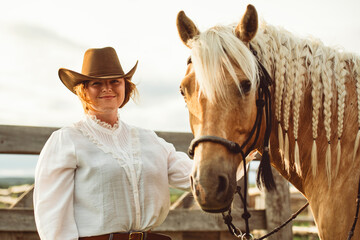 A woman, proudly wearing a cowboy hat, stands next to her horse