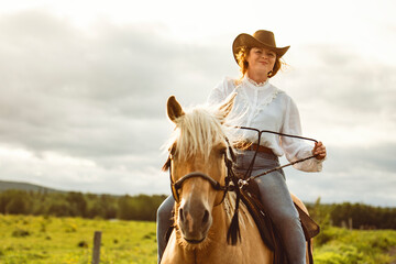 A woman is wearing a cowboy hat while riding a horse in an open field