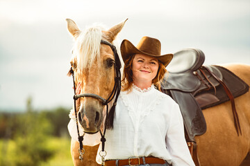 A woman, proudly wearing a cowboy hat, stands next to her horse