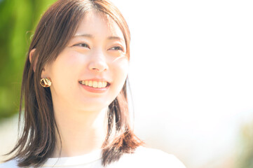 逆光の中で柔らかな笑顔を見せる白いシャツの若い女性のポートレート