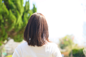自然豊かな背景の中で後ろ姿を見せる短髪の若い女性