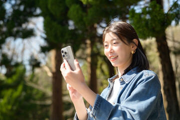 スマートフォンを見ながら穏やかに笑う女性の春の屋外シーン