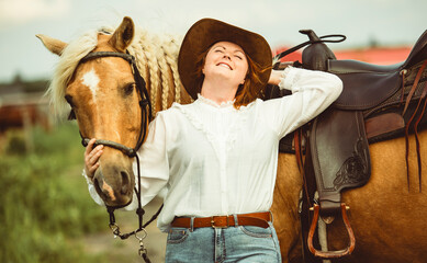 A woman, proudly wearing a cowboy hat, stands next to her horse