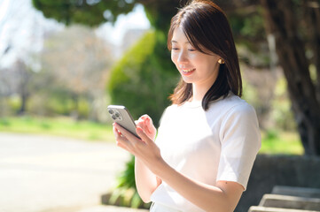 木漏れ日の中でスマホを手にした女性が春の空気を感じながら歩く様子