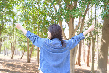春の森林の中で両手を広げて立つ女性の後ろ姿が開放感を表現する