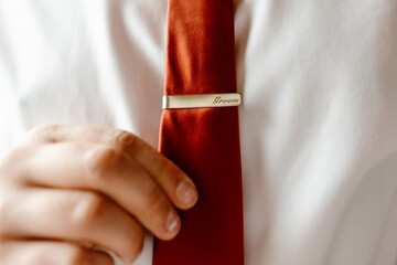 Elegant man putting tie bar on red tie