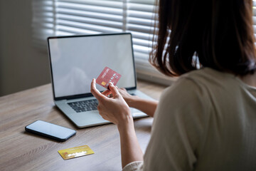 A woman is holding a credit card in front of a laptop