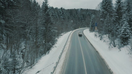 Aerial view of a winding snowy mountain road cutting through a dense winter forest. Mountain road...