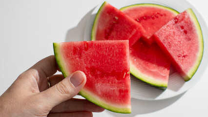 Sliced watermelon, held by a fair-skinned hand, conjures summer picnics and the quirky...