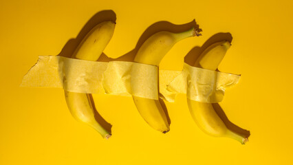 Duct-taped bananas against bold yellow canvas, quirky art installation embodies absurdity, Banana Day celebration, pop-art whimsy