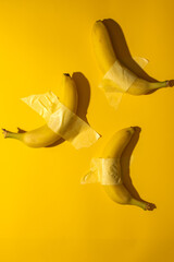 Taped bananas defy gravity on vivid yellow, playful nod to Dadaism and National Fruitcake Toss Day whimsy