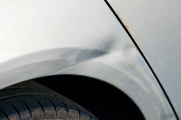 Car rear fender with visible dent and paint scratches from minor collision or scrape, common vehicle body damage. Scratched car closeup. Fender of vehicle with chipped paint, surface scratches, dent