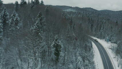 Aerial view of a winding snowy mountain road cutting through a dense winter forest. Mountain road...