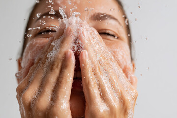 Fototapeta premium Hands splashing foamy facial cleanser on face with water droplets in mid-motion