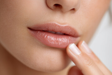 Cropped close-up of hand applying clear lip balm to natural lips on soft background