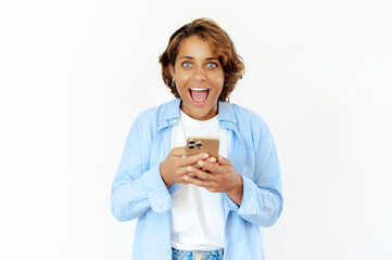 Shocked blue-eyed brazilian young adult woman enthusiastically using smartphone, reacting with big...
