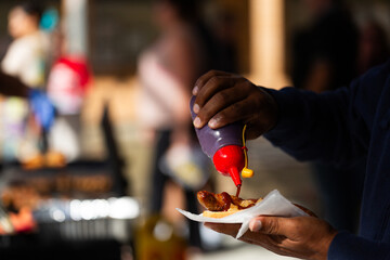 Man pouring bbq sauce at on sausage and bread held in hand on election day
