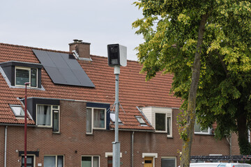 A Dutch street scene featuring residential houses with solar panels on a tiled roof and a speed...