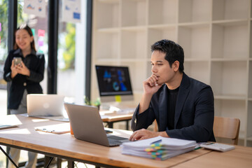 Obraz premium A man is sitting at a desk with a laptop and a stack of papers