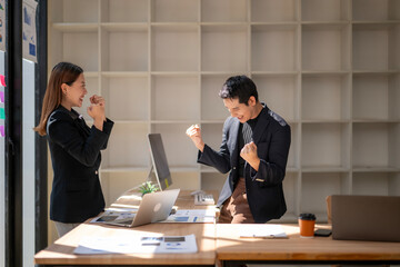 A man and a woman are standing in front of a desk with a laptop and papers